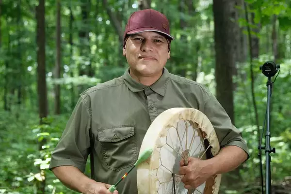 Photo of Shauit in a dark green shirt and red cap, stood in a forest