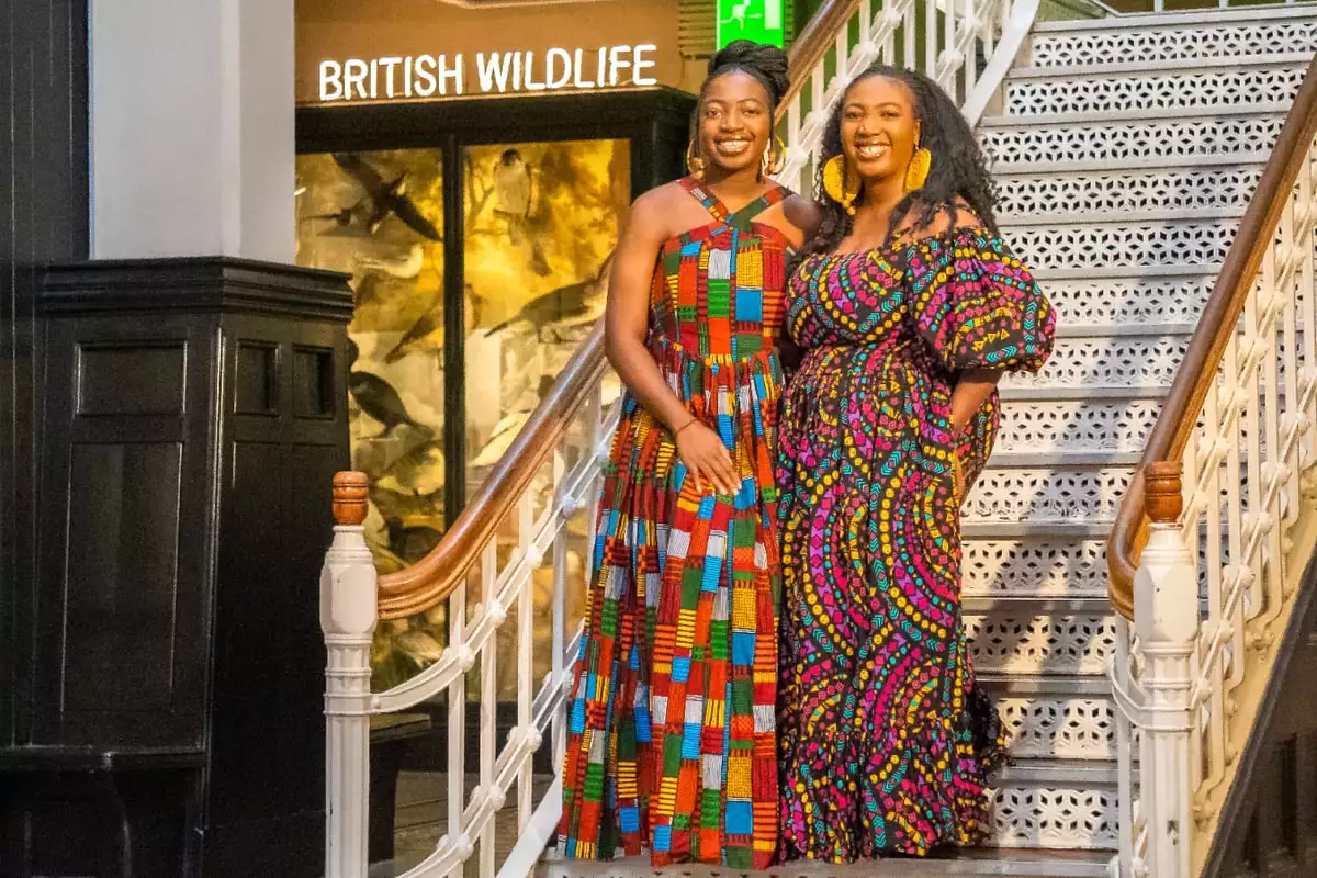 Adeola and Ronke Jane Adelakun smiling, wearing colourful dresses in a Museum setting