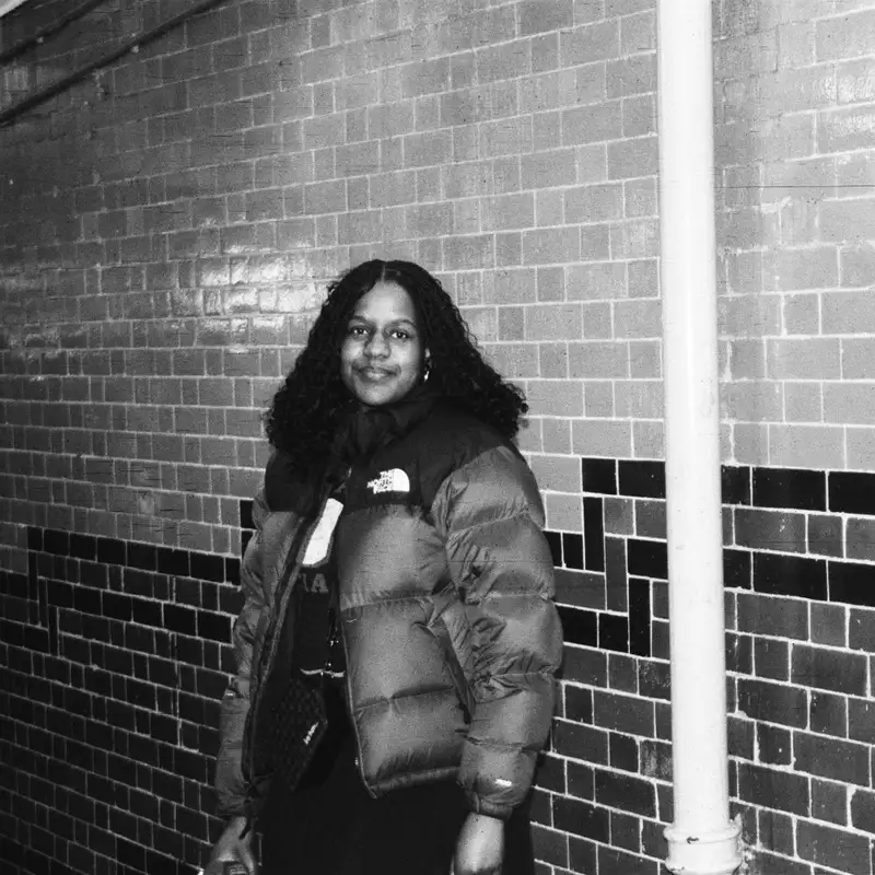 Black and white photo of someone stood against a brick wall