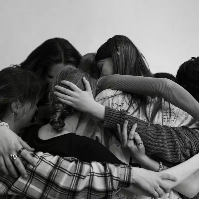 A black and white photograph of young people with their arms around each other in a group cuddle