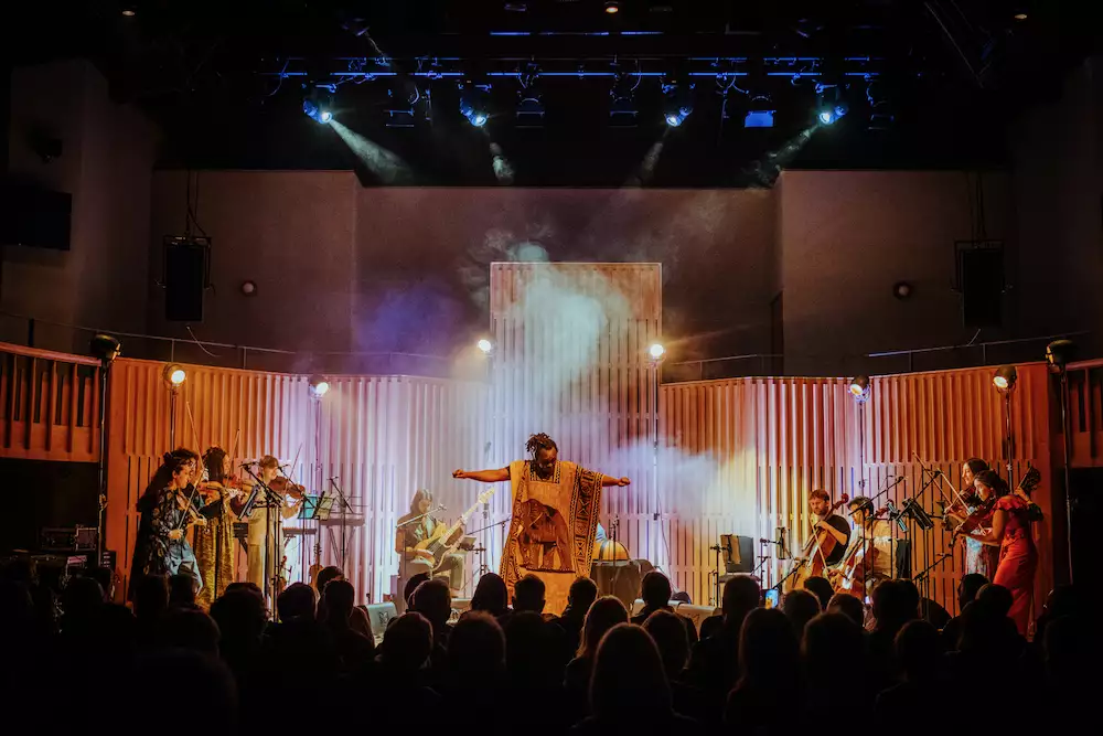 Manchester Collective and Abel Selaocoe performing on stage with orange lighting and a crowd watching