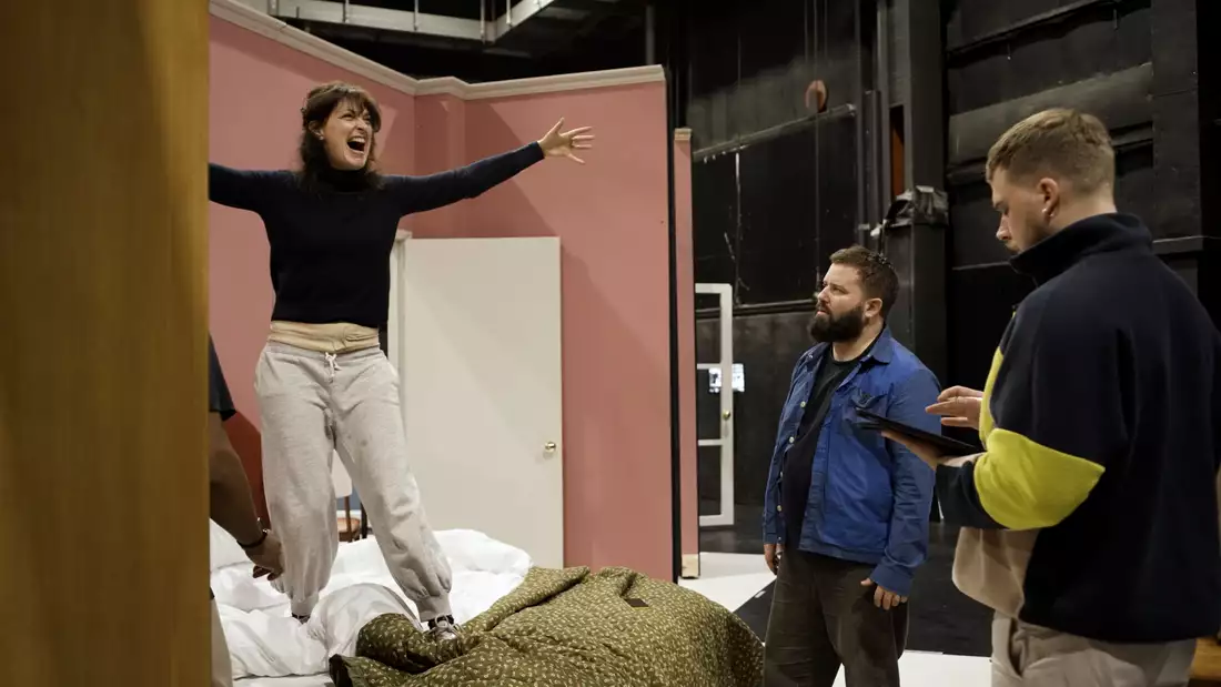 Kip Williams directing two people on the set of Angel's Bone. A woman is standing on a bed singing.