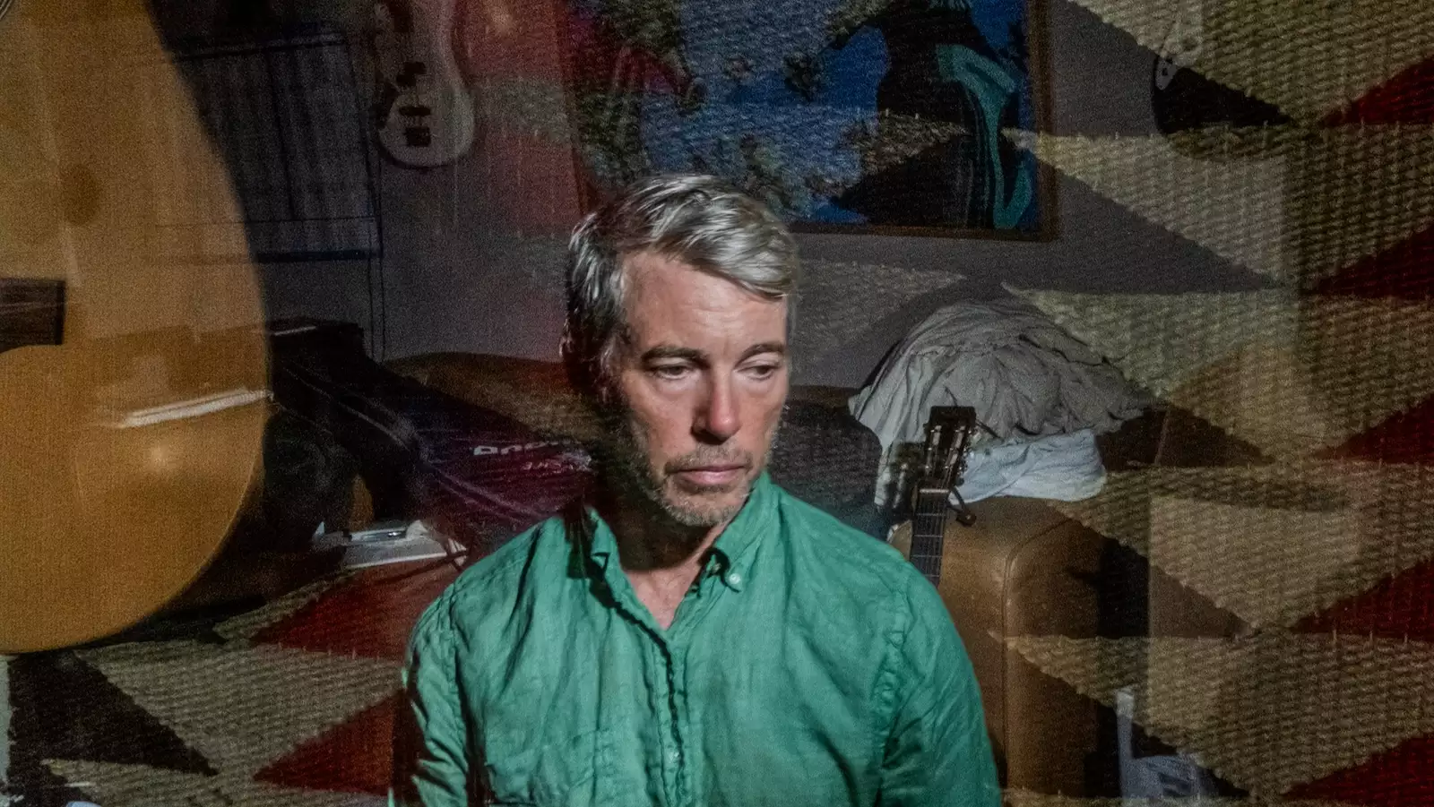 Bill Callahan wearing a green shirt sitting indoors, overlaid with a double exposure of a guitar and patterned rug.