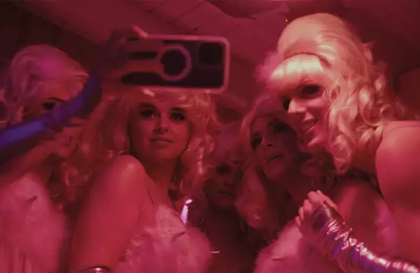 A still from A House Is Not A Disco, showing a group of people dressed up and taking a selfie. The image has a pink hue.
