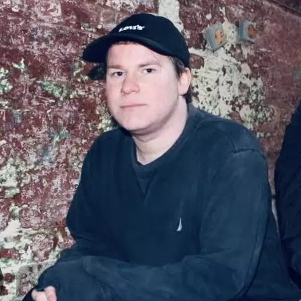 Headshot of Jake Talbot sat in front of a wall wearing a cap