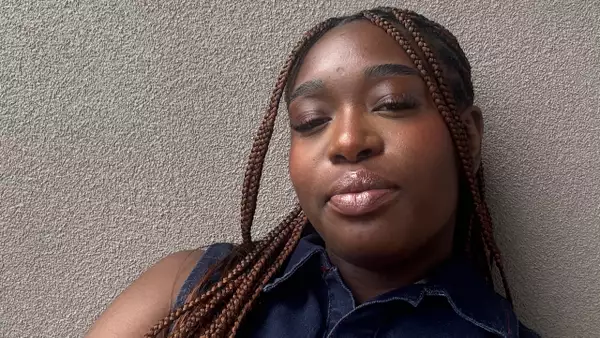 Adele Tondu wearing a denim top leaning against a grey wall