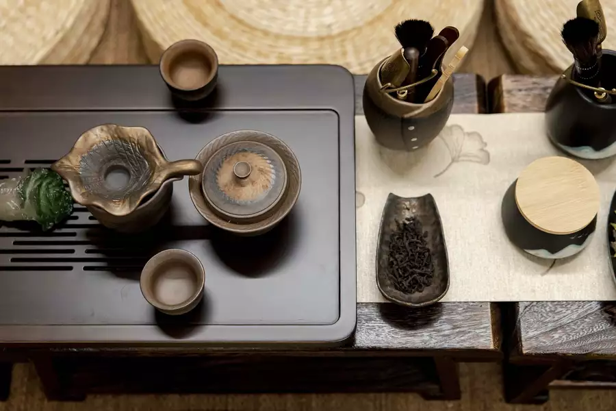 Traditional tea setup with teapot, cups, tea leaves, and tools arranged on a wooden tray.