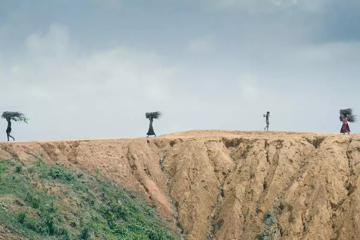 Five people walking across a dry landscape carrying sticks