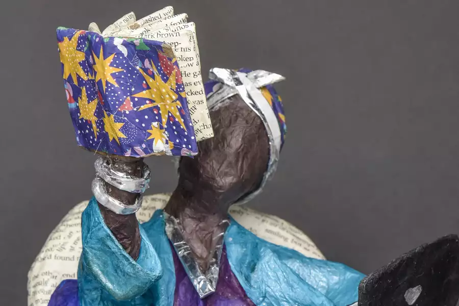 A papier mache figure holding a papier mache book