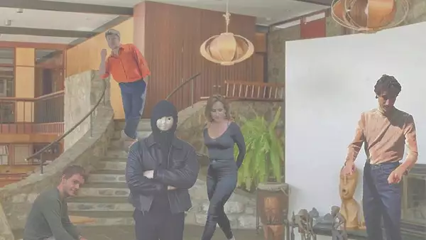 Five people pose in a modern, mid-century style interior: one leans on a staircase, another crouches, one wears a hood and mask, one stands by plants, and another touches a wooden sculpture. Warm lighting and stone walls.