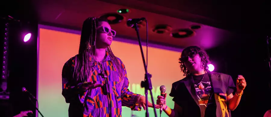 Two people performing on stage wearing brightly coloured clothing