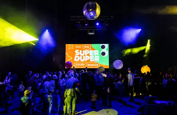 A large crowd of families dancing in the Warehouse with a screen that reads 'Super Duper Family Festival'