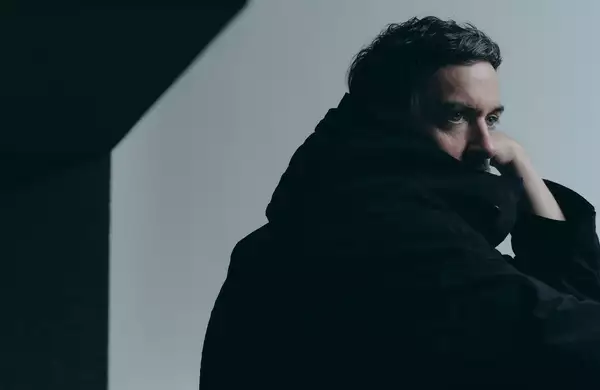 Bonobo wearing a black jacket looking to the side, with a shadow on the wall behind him