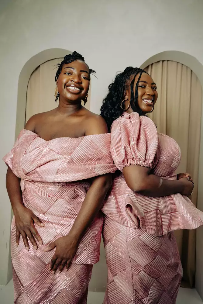 Adeola and Ronke Jane Adelakun smiling and wearing matching light pink dresses