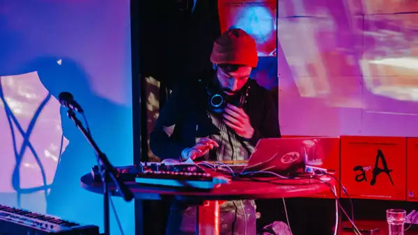 Astrolayb performing on a stage surrounded by a mic, laptop and music equipment