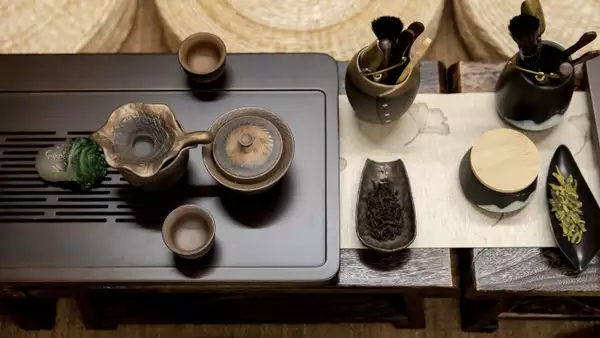 Traditional tea setup with teapot, cups, tea leaves, and tools arranged on a wooden tray.