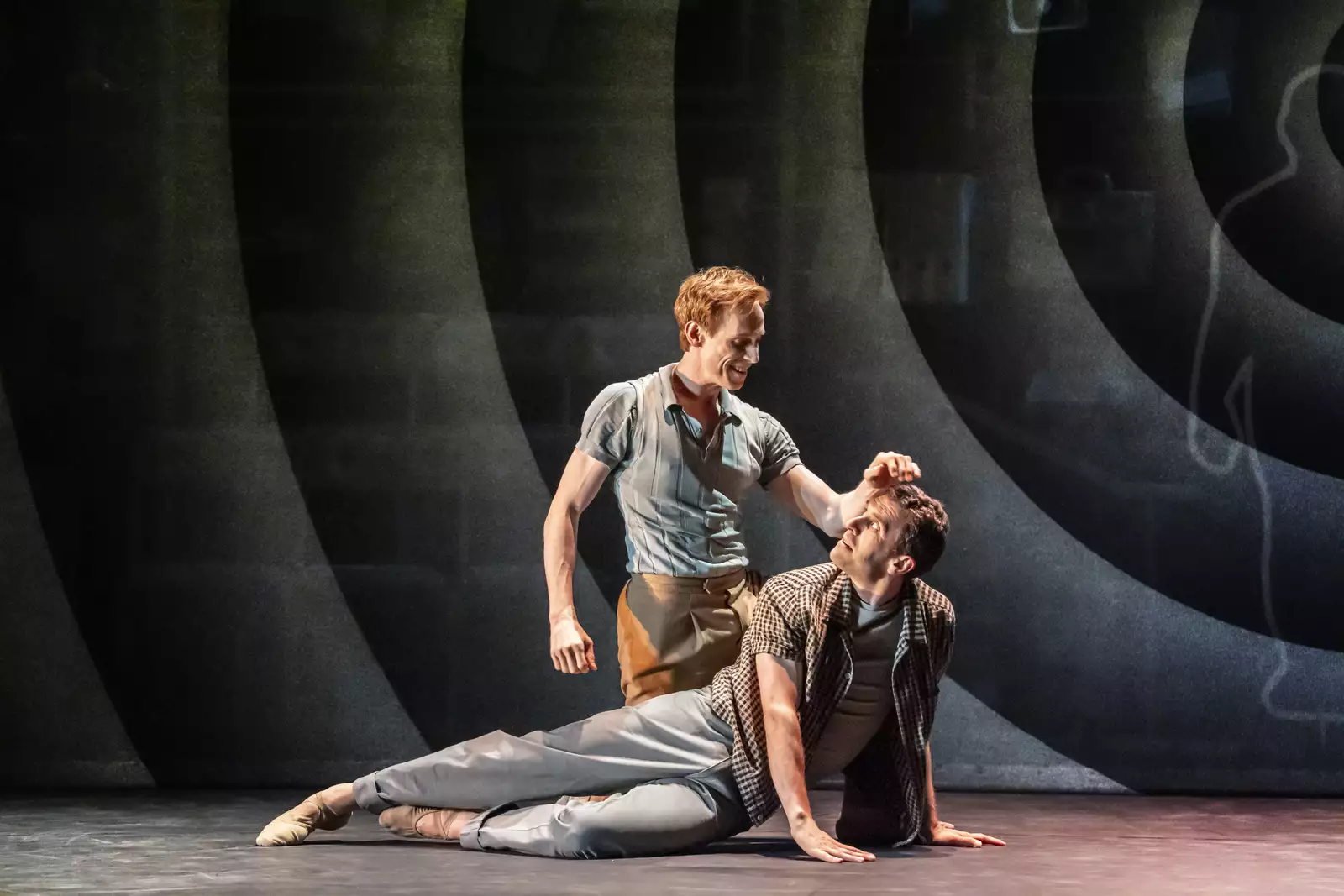 A photo of two ballerinas, one lying on the ground the other leaning over him