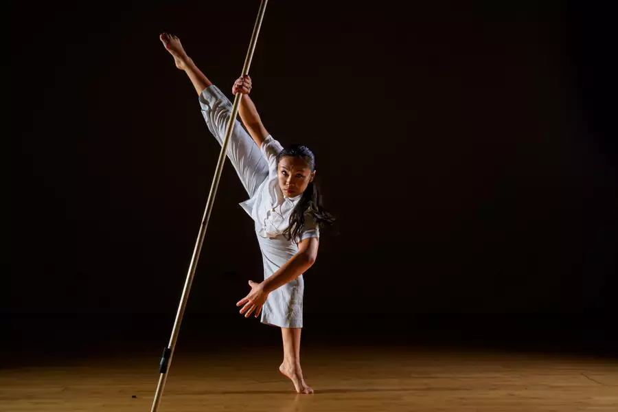 A dancer on a dimly-lit stage dancing with a large pole