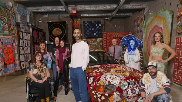 Hetain Patel standing in an exhibition with his artwork made from a car, with other people around him