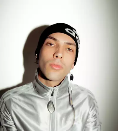 Jack Jameson wearing a silver velvet Adidas hoodie and a black hat, on a white background