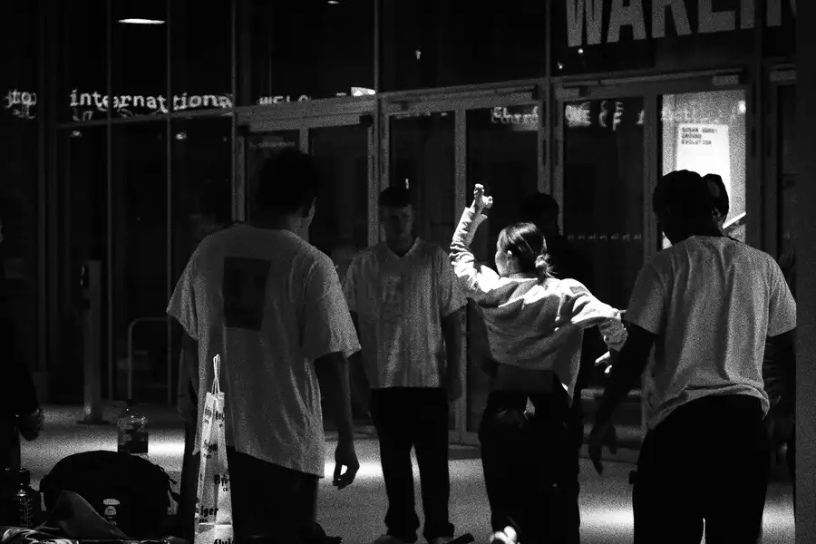 A black and white photograph of a group of people in the Social, which is dimly lit. One person is energetically dancing while others watch.