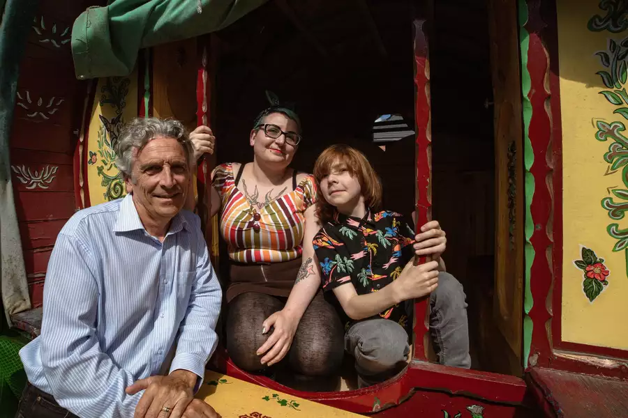 A man, a woman and a child pose together in the doorway of a brightly painted traditional wooden caravan. Floral and bird designs decorate the caravan’s exterior.