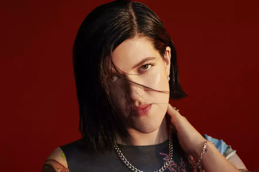 A close up photograph of singer, songwriter and producer Romy looking at the camera against a dark red background