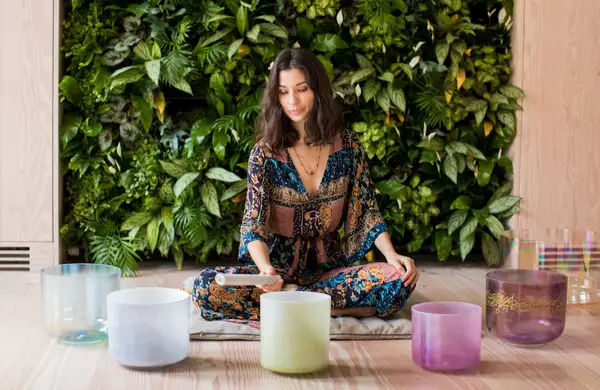 A person leading a sound bath in front of a wall of grass