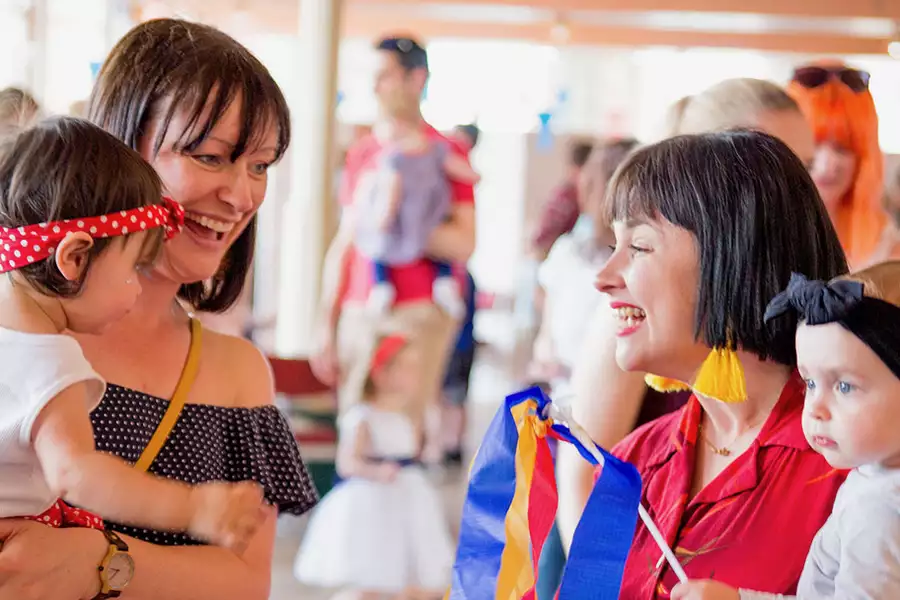 Two parents holding their toddlers and smiling. The toddlers are wearing headbands.