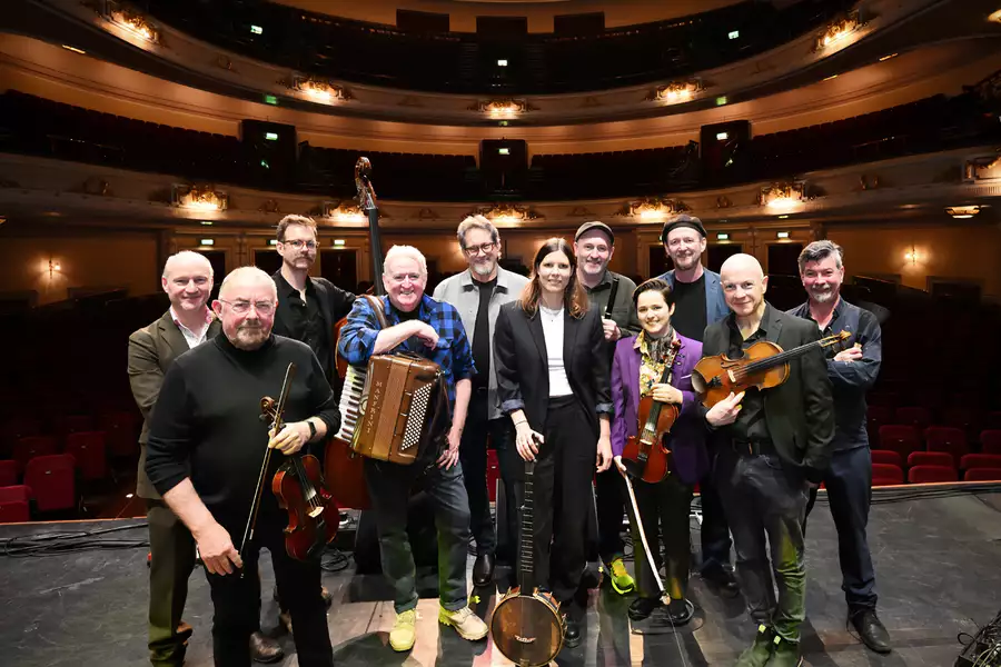Members of Transatlantic Sessions stood on stage with their instruments. There is an empty auditorium behind them.