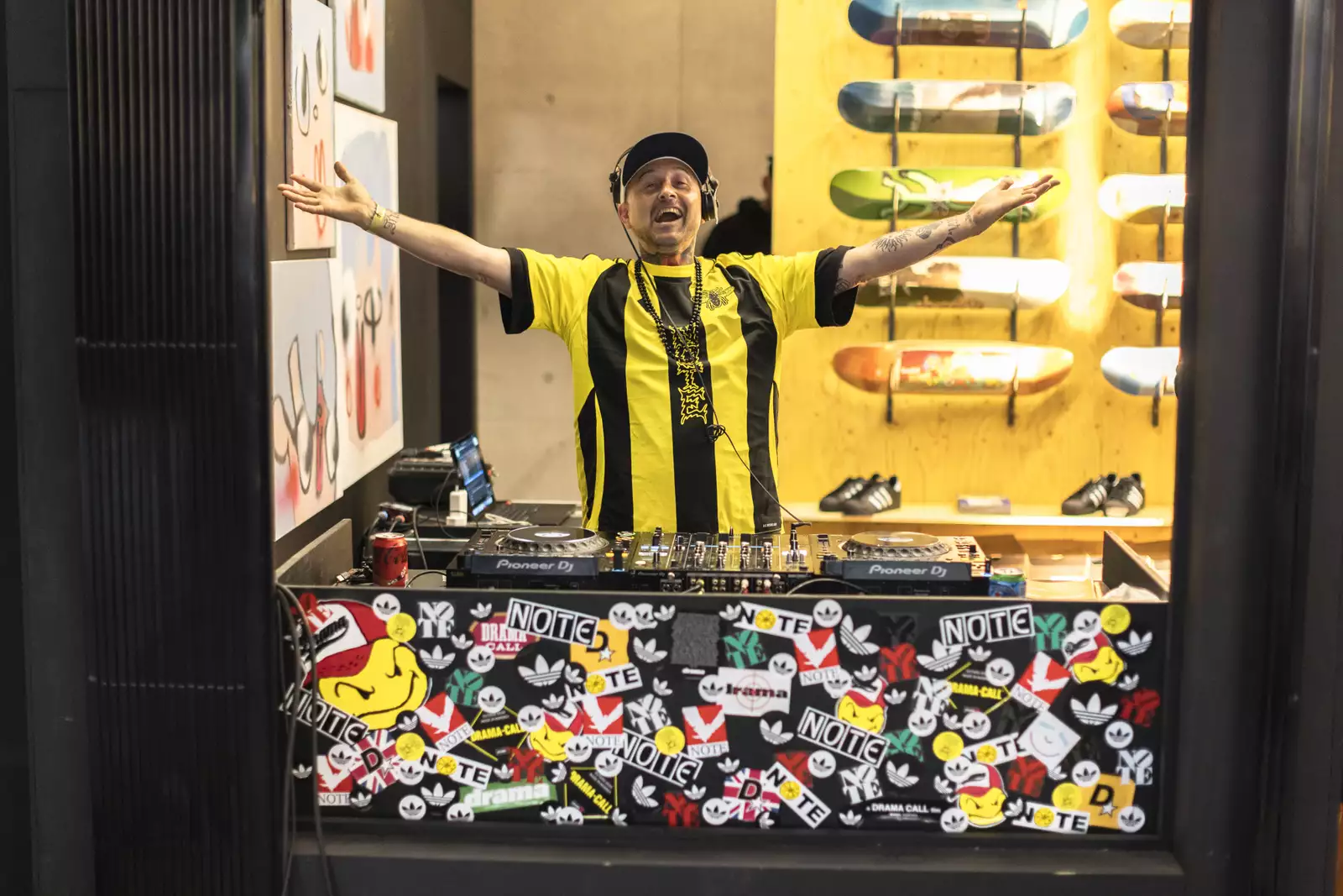 A person DJing inside a pop-up skate shop as part of Build Manchester. They are wearing a yellow and black striped football shirt.
