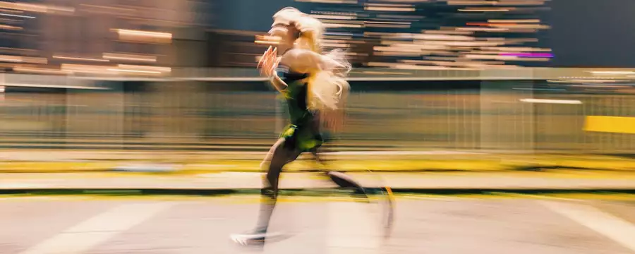 A runner sprints through a city at night, captured in motion blur against streaks of urban lights. The dynamic movement and glowing cityscape create a sense of speed and determination.