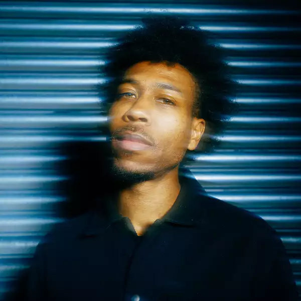 Obeka looking towards the camera. He is stood against a shutter.