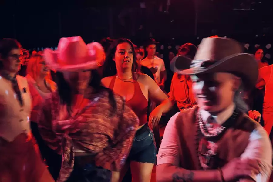 Blurry photo of a crowd of people dancing wearing cowboy hats. The lighting is red.