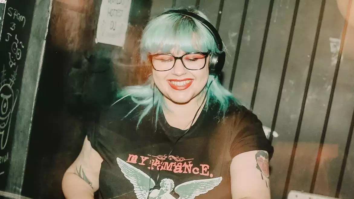 Mx World DJing with bright blue hair and wearing a My Chemical Romance t-shirt