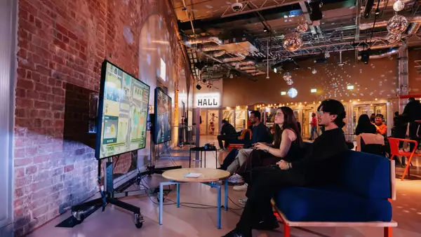 Two people playing on the playstation in the Social. The lighting is dim and disco balls are on display.