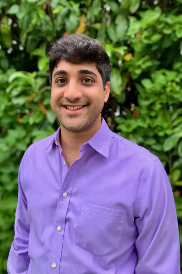Jai Morjaria wearing a bright purple shirt in front of a green hedge