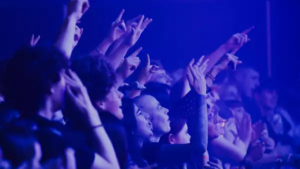 A crowd of people cheering and filming over the barrier in the Warehouse at Aviva Studios. The lighting is blue.