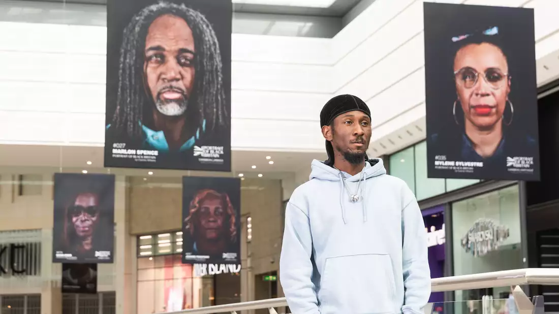 Cephas Williams is photographed standing among his photographs, which are hanging from the ceiling at the Arndale Centre in Manchester.