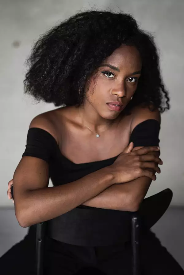 Headshot of Marie-Astrid Mence wearing a black top, sat on a black chair