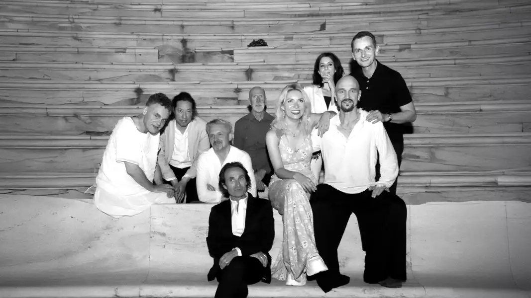 Nine members of James sitting and standing on stone steps. The image is black and white. They are casually dressed, some in light-colored clothes, with one person in a dress, and others in shirts or casual attire.