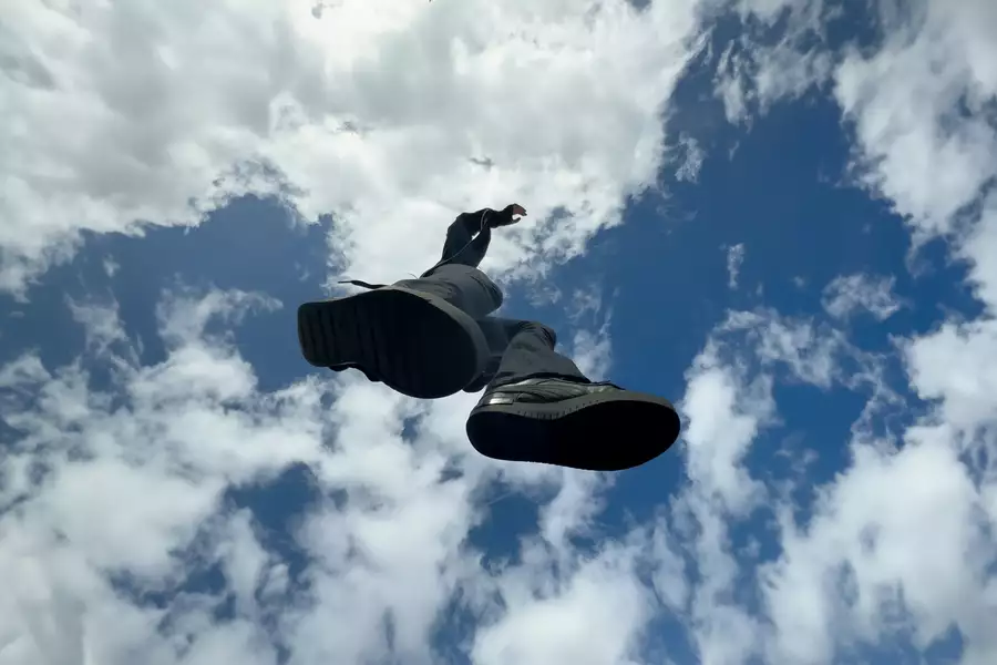 A photograph taken from underneath a child jumping. The sky is bright blue with some clouds.