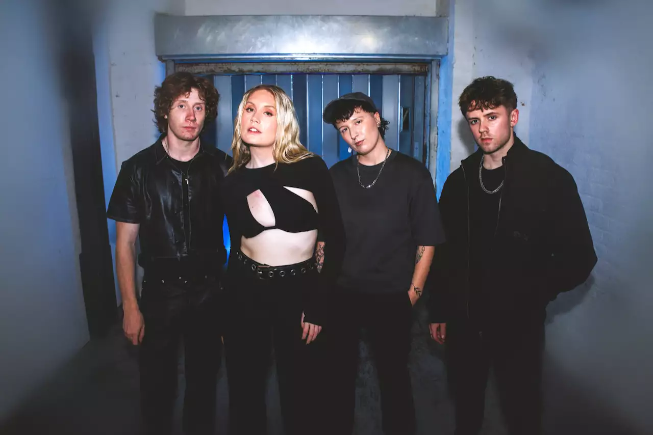 Four members of PAVE wearing all black clothing. The background shows a bare, industrial room.