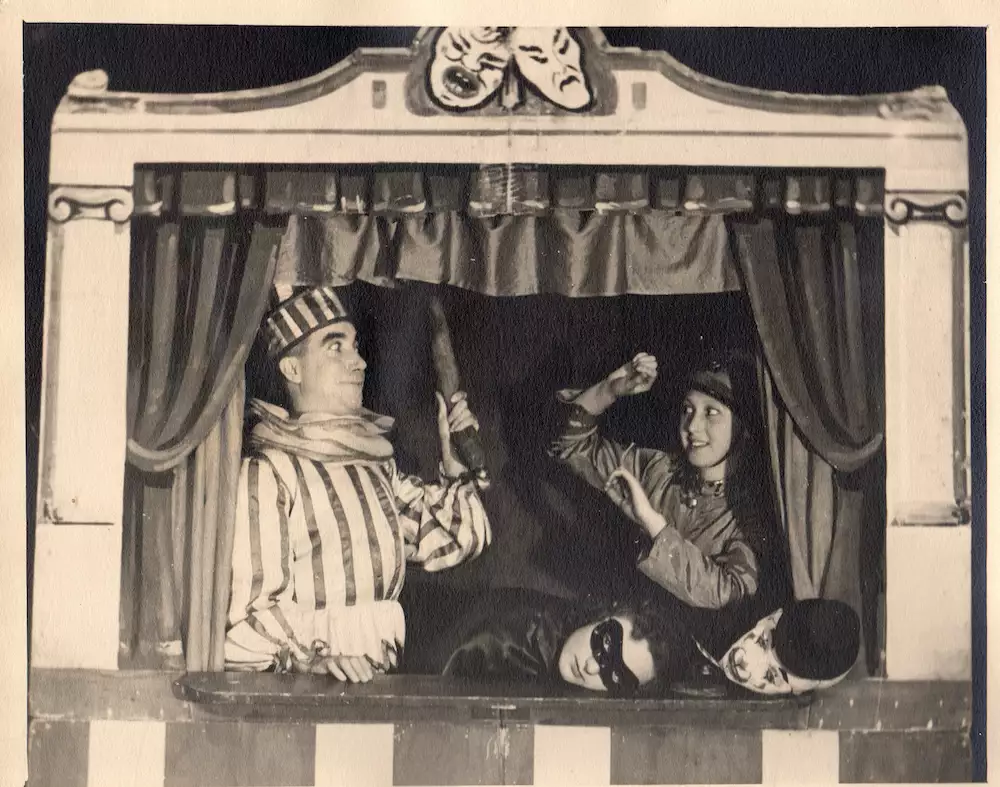 Two costumed performers act inside a small puppet theatre