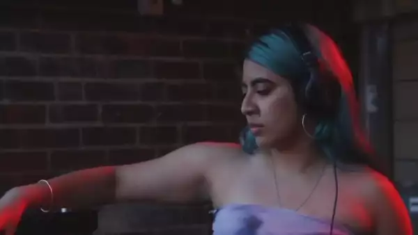 Lotus Phase with headphones on DJing. They are wearing a purple top and a silver bangle on their wrist.