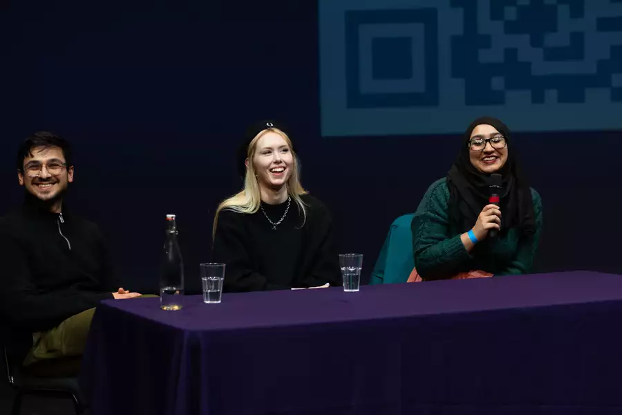 Three people smiling during a panel talk. One is speaking into a microphone.
