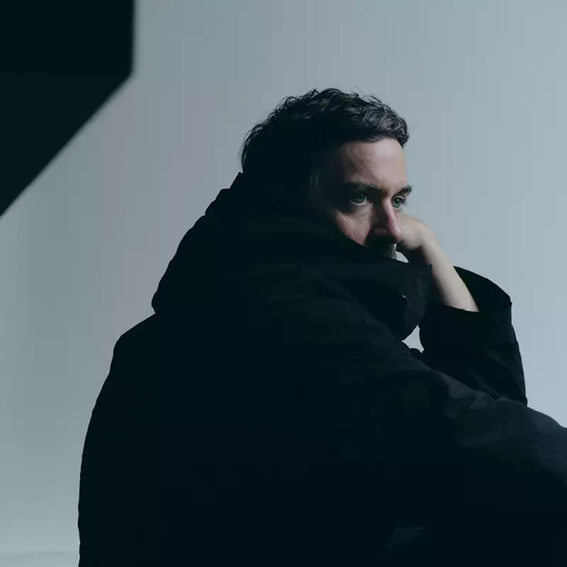 Bonobo wearing a black jacket looking to the side, with a shadow on the wall behind him