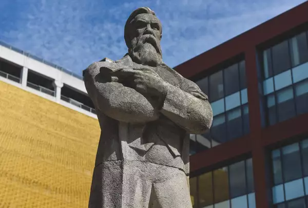 Image of the decommissioned statue of Engels with a blue sky and a yellow building behind