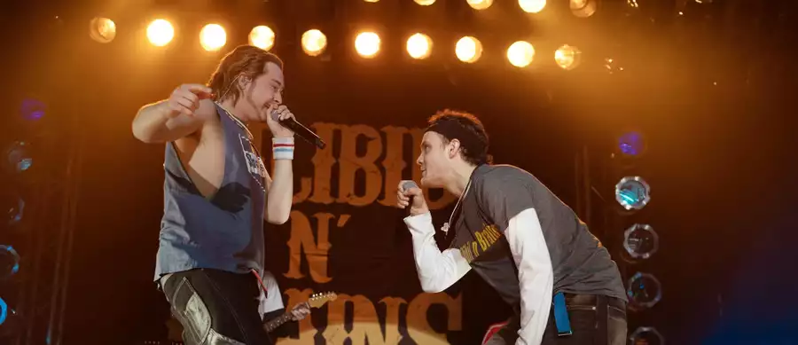 A still from California Schemin' showing two men on stage singing into a microphone