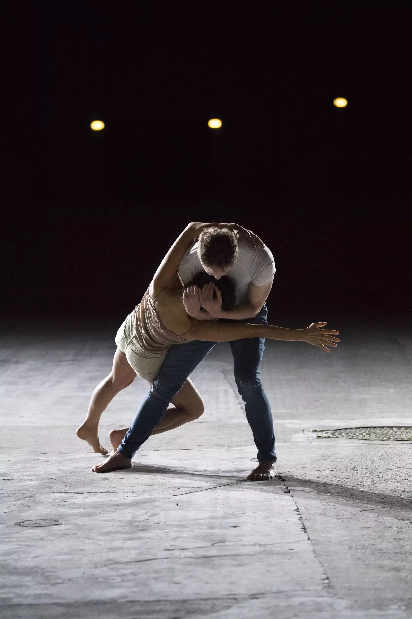 Two dancers embrace on a concrete floor